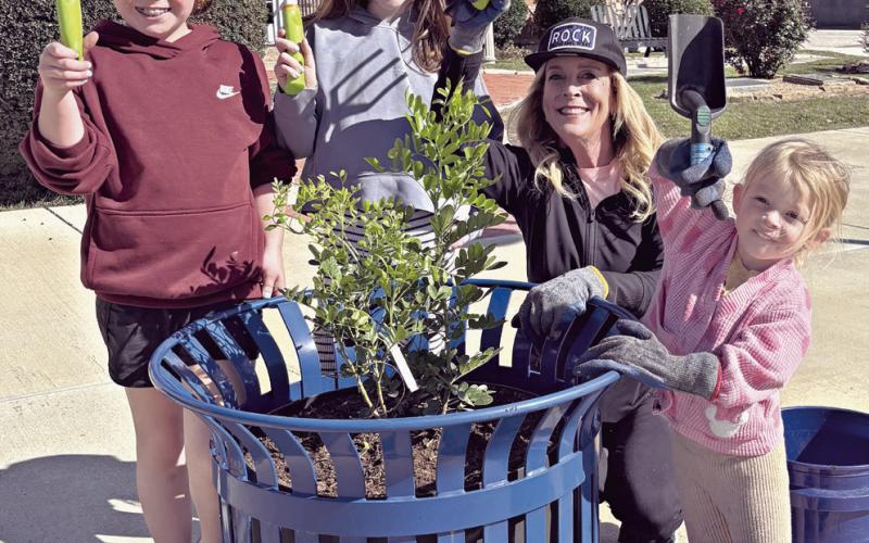 At right, Kathryne Roddam teaches her granddaughters early about volunteering by planting Texas Mountain Laurels in downtown planters. Shown here (L-R) are Caroline, Grace, Roddam and Hannah.