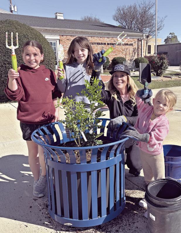 At right, Kathryne Roddam teaches her granddaughters early about volunteering by planting Texas Mountain Laurels in downtown planters. Shown here (L-R) are Caroline, Grace, Roddam and Hannah.