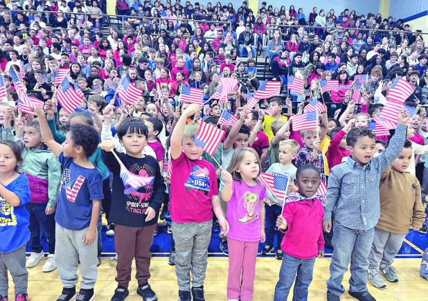 TRIBUTE TO VETERANS— RISD held its annual Veterans Day program last week and bused all students to the high school gym for an hour-long salute to Rockdale’s veterans. Above, the elementary students singing “You’re a Grand Old Flag” while waving flags. See more photos on page 10A.