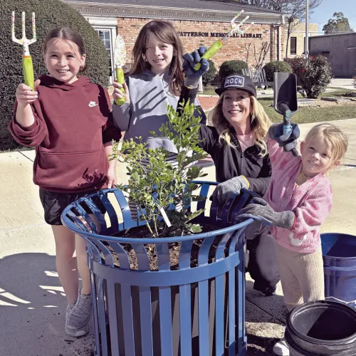 At right, Kathryne Roddam teaches her granddaughters early about volunteering by planting Texas Mountain Laurels in downtown planters. Shown here (L-R) are Caroline, Grace, Roddam and Hannah.