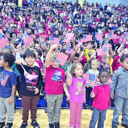 TRIBUTE TO VETERANS— RISD held its annual Veterans Day program last week and bused all students to the high school gym for an hour-long salute to Rockdale’s veterans. Above, the elementary students singing “You’re a Grand Old Flag” while waving flags. See more photos on page 10A.